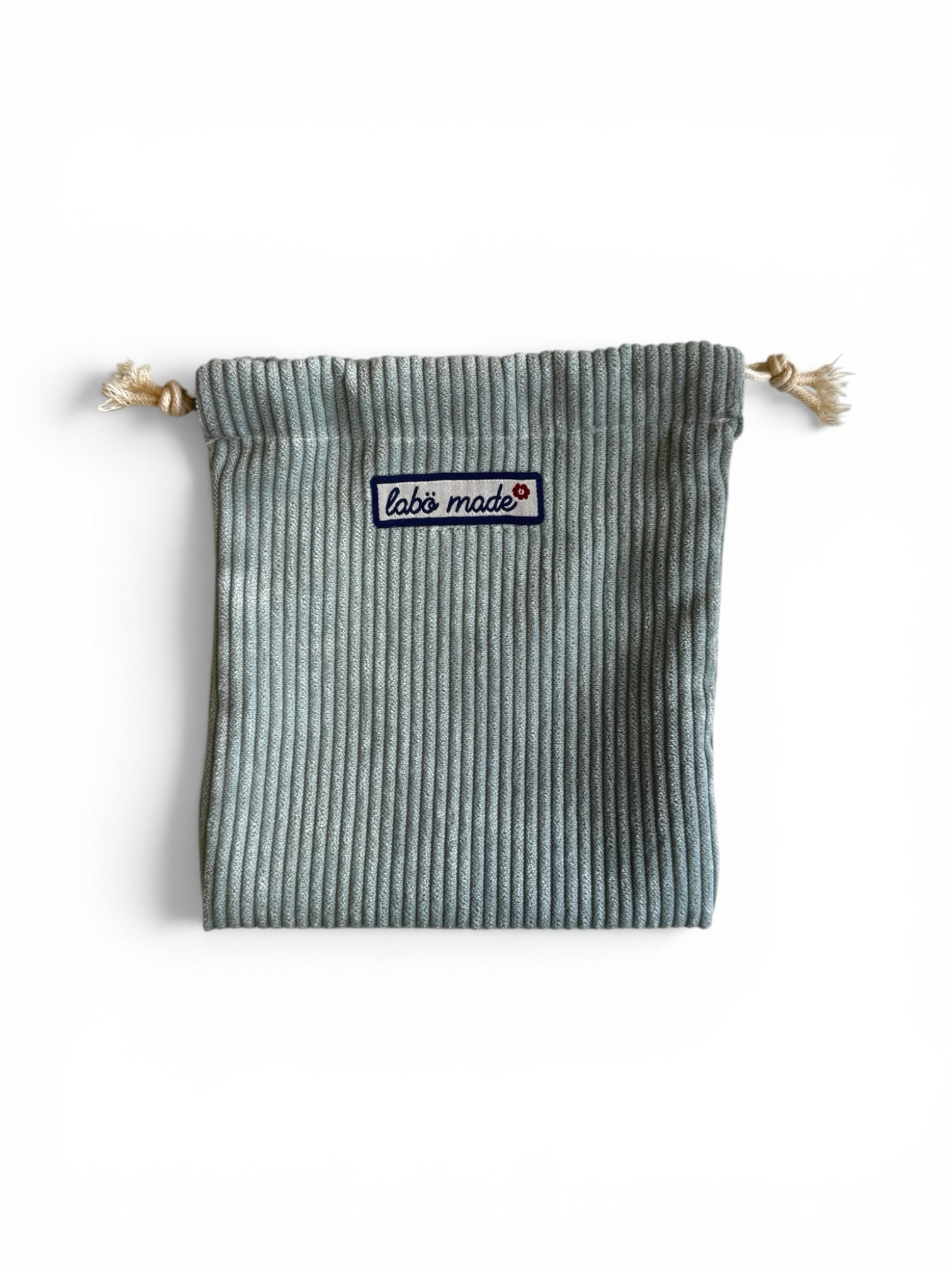 Labö Made sage green corduroy drawstring pouch with a branded woven patch, perfect for organising small essentials.